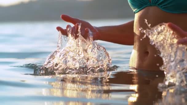 CLOSE UP: Жінка-туристка бризкає воду під час охолодження в океані на заході сонця
 - Кадри, відео