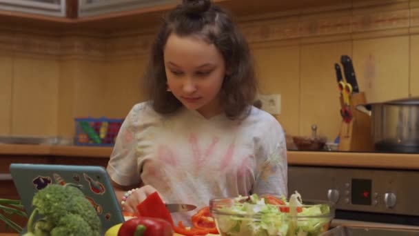 Adolescente chica preparando ensalada mira el video receta en una tableta digital - Imágenes, Vídeo
