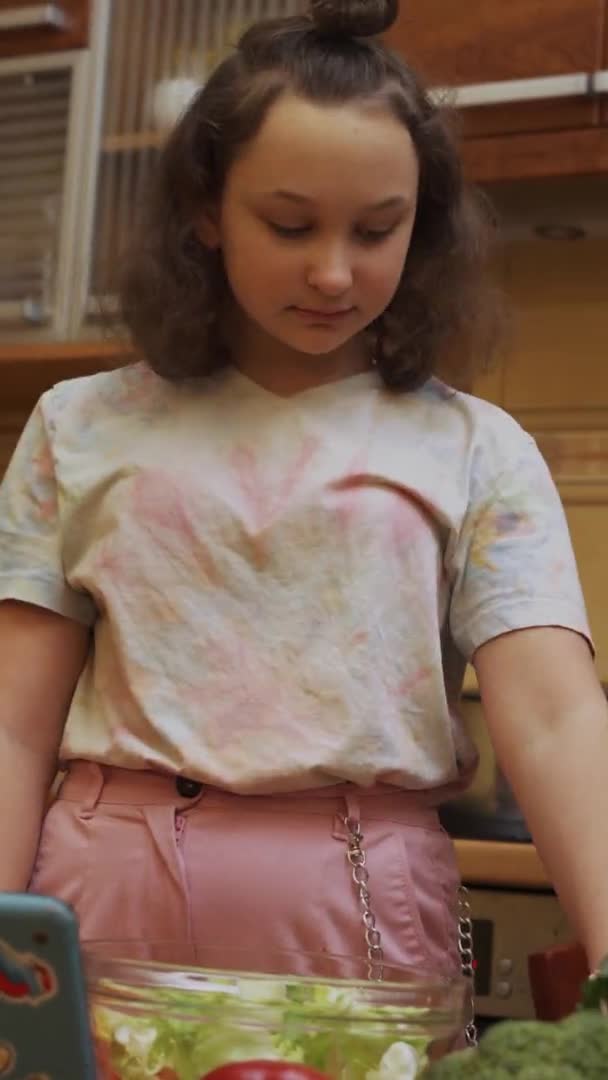 Chica adolescente preparando ensalada con tableta digital. Formato vertical - Imágenes, Vídeo