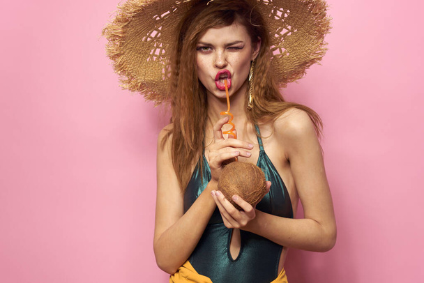Žena s kokosovým koktejlem v ruce plavky plážový klobouk kosmetika luxusní životní styl růžové pozadí - Fotografie, Obrázek