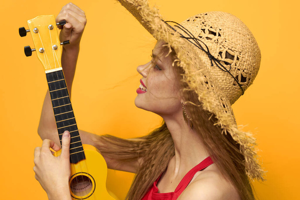 Mujer sosteniendo Ukulele sombrero de paja estilo de vida Fondo amarillo exótico - Foto, imagen