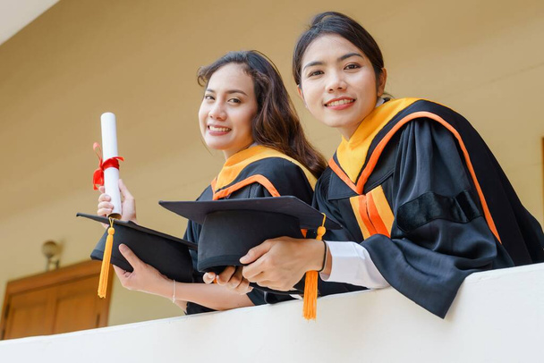 Os graduados universitários em vestido de graduação e um boné de papelão com um certificado de grau na mão celebrando a realização da educação na cerimônia de início. Parabéns às formaturas - Foto, Imagem