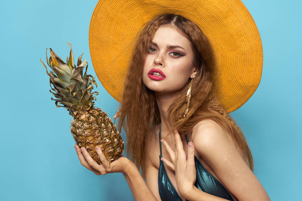 女性でビーチハットパイナップル保持水着エキゾチックなフルーツ青背景休暇 - 写真・画像