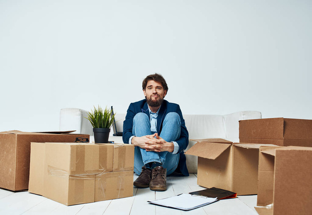 Ο άνθρωπος κάθεται στο πάτωμα με τα κουτιά των πραγμάτων κινείται στο γραφείο ξεπακετάρισμα τρόπο ζωής - Φωτογραφία, εικόνα