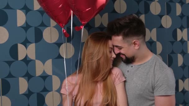 Caucásico hombre está abrazando a su amante en una pared azul sonriéndole mientras que da aire globos rojos - Metraje, vídeo