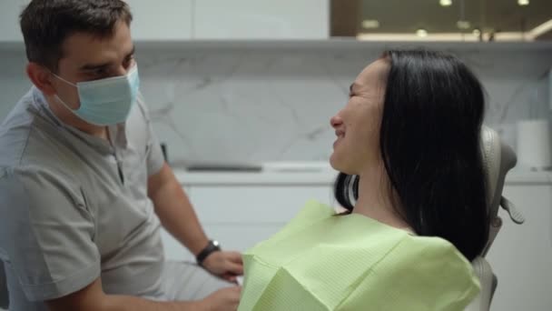 Giovane donna caucasica all'appuntamento medico siede sulla sedia dentale e apre la bocca. Il medico fa un esame visivo dei denti. - Filmati, video