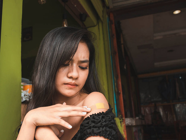 Een mooi Filipijns meisje is geïrriteerd over een kleine wond bedekt met een pleister dat een litteken of vlek op haar schouder kan veroorzaken.. - Foto, afbeelding