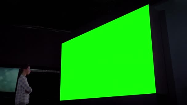 Женщина смотрит на большой пустой зеленый экран в темной комнате - концепция хрома ключ - Кадры, видео