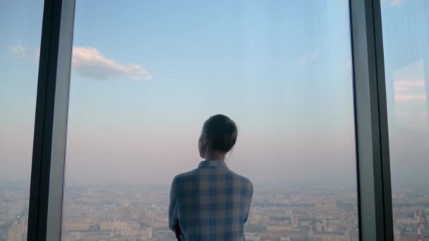 Pensive nainen katselee kaupunkikuva ikkunan läpi pilvenpiirtäjä - peruutusnäkymä - Materiaali, video