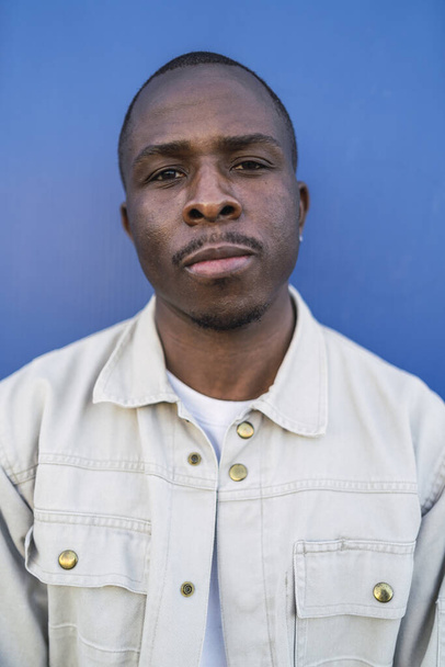 A vertical portrait of a Black young male on a blue background - Zdjęcie, obraz