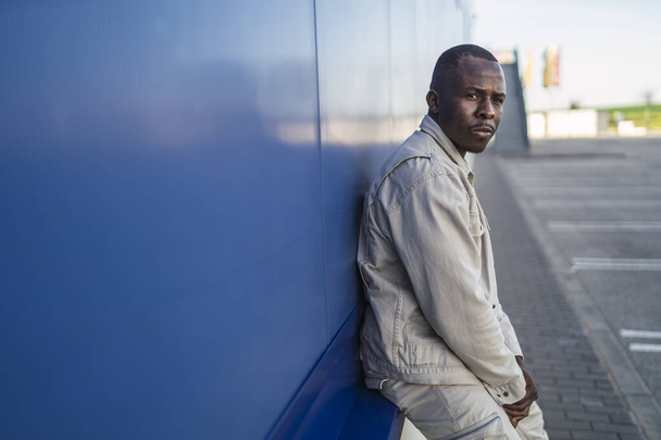 A closeup shot of a Black young male standing in front of a blue wall - Foto, imagen