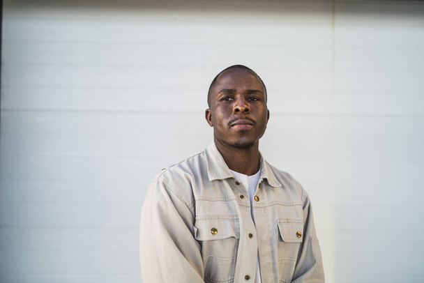 A closeup shot of a Black young male standing outdoors in front of a white wall - Foto, Bild
