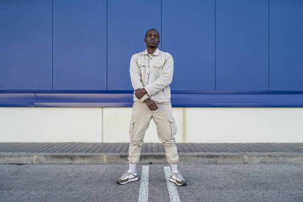 A closeup shot of a Black young male standing in front of a blue wall - Photo, image