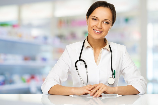 Giovane donna medico bruna positiva dietro il tavolo in farmacia
  - Foto, immagini