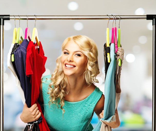 Sorridente donna bionda che sceglie i vestiti su un rack in un centro commerciale
   - Foto, immagini