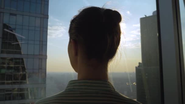 Umsichtige Frau betrachtet Stadtbild durch Fenster eines Wolkenkratzers - Rückansicht - Filmmaterial, Video
