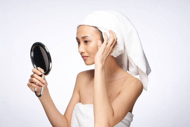 femme d'apparence asiatique avec un miroir dans ses mains peau claire épaules nues fond clair - Photo, image