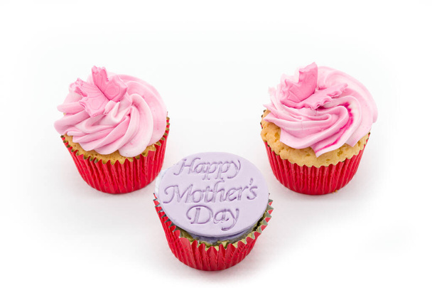 Tres pasteles de taza con glaseado rosado y tripas de esponja roja sobre un fondo blanco. Con el Día de las Madres Felices, en el pastel de la taza delantera. - Foto, imagen