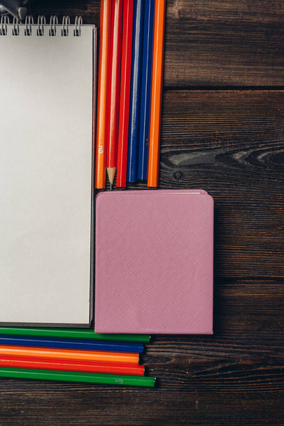 notatniki kolorowe ołówki i papeteria w szklance na drewnianym stole widok z góry - Zdjęcie, obraz
