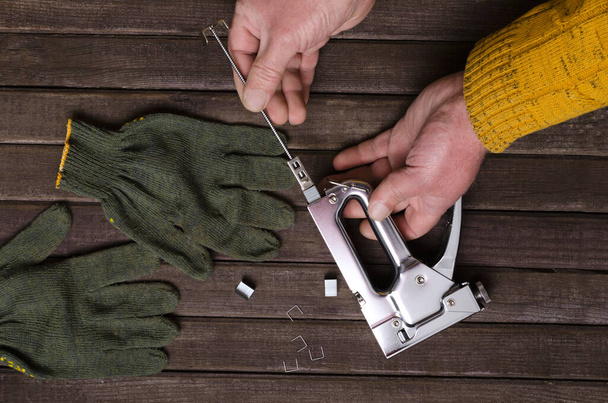 男性の手、金属の主食銃、木製の表面に手袋のトップビュー。家具を固定するための準備のプロセス - 写真・画像
