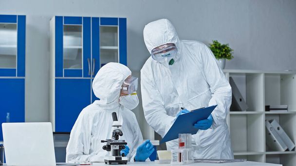 scientist in hazmat suit showing research results to colleague in laboratory - Photo, Image
