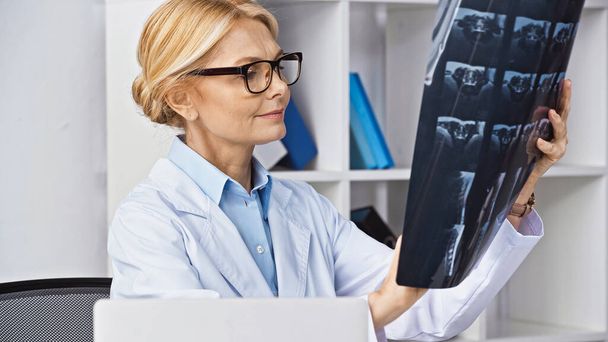 блондинка-лікар в окулярах дивиться на рентген в клініці
 - Фото, зображення
