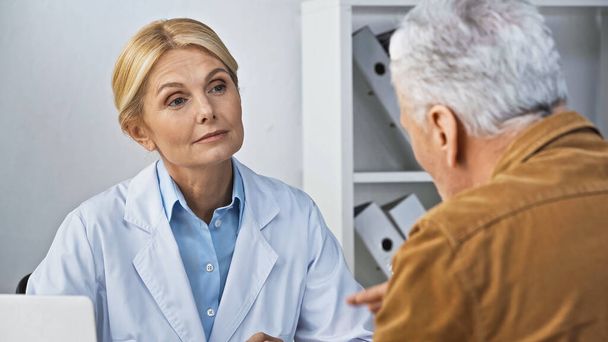 atento médico escuchando al hombre durante la consulta en el hospital, borrosa primer plano - Foto, Imagen