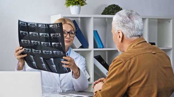 arts toont röntgenfoto aan patiënt tijdens consultatie in ziekenhuis - Foto, afbeelding