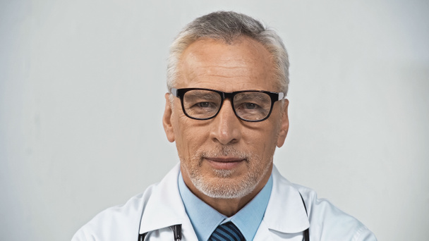 positiver, reifer Arzt mit Brille, der im Krankenhaus in die Kamera lächelt - Foto, Bild