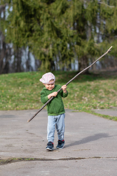 Een jongen rent de natuur in met een houten stok. Kleine jongen spelen met stok in het bos  - Foto, afbeelding