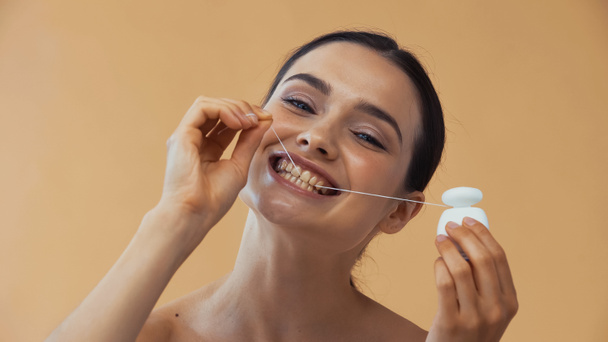 junge Frau mit Zahnseide, während sie isoliert auf beige in die Kamera blickt - Foto, Bild