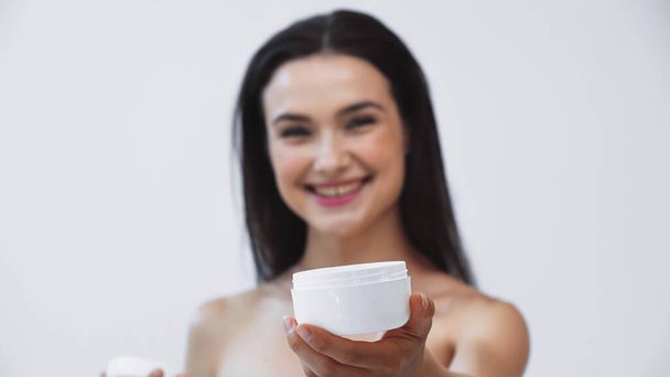 mulher feliz mostrando recipiente de creme cosmético no fundo borrado isolado no cinza - Foto, Imagem