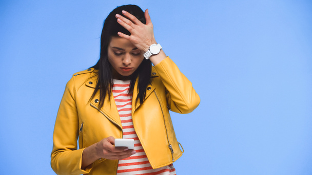 inquiet jeune femme messagerie sur smartphone isolé sur bleu - Photo, image