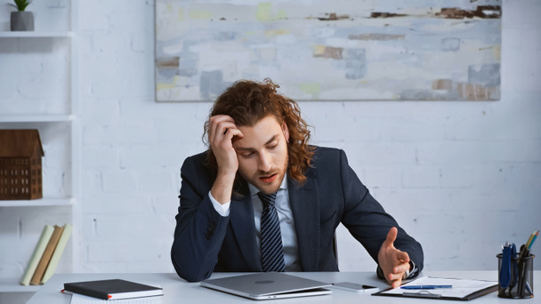 homem de negócios cansado apontando para smartphone enquanto sentado no local de trabalho - Foto, Imagem