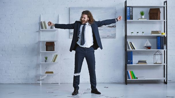 full length view of excited businessman showing success gesture near falling dollar banknotes - Photo, Image
