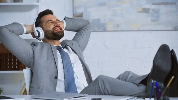 happy businessman listening music in headphones while relaxing in office - Photo, Image