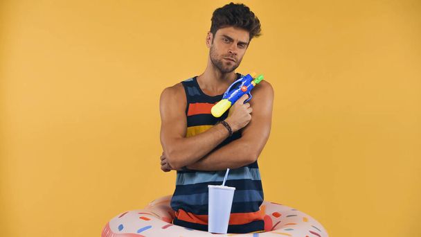 muž v nafukovacím kruhu drží vodní pistole izolované na žluté - Fotografie, Obrázek