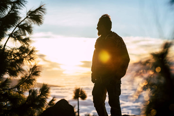 Yetişkin bir adam ayakta ve gün batımına bakıyor. Özgürlüğün ve sağlıklı yaşam tarzının tadını çıkarıyor.  - Fotoğraf, Görsel