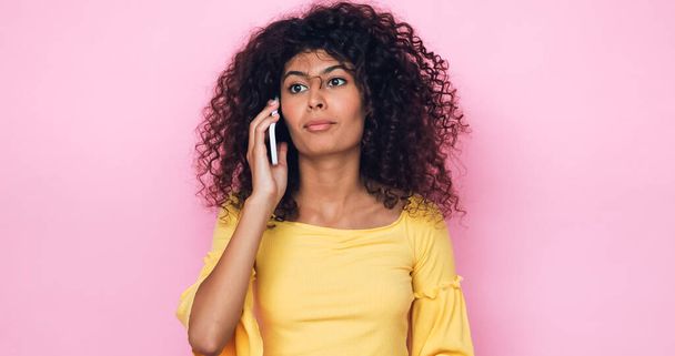 rizado mujer joven hablando en el teléfono móvil aislado en rosa - Foto, imagen