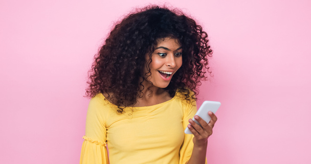 mujer joven positiva sosteniendo teléfono móvil aislado en rosa  - Foto, imagen