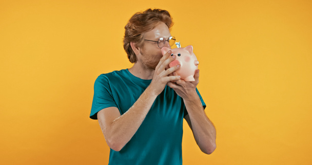 zrzka muž v brýlích líbání prasátko banka izolované na žluté  - Fotografie, Obrázek