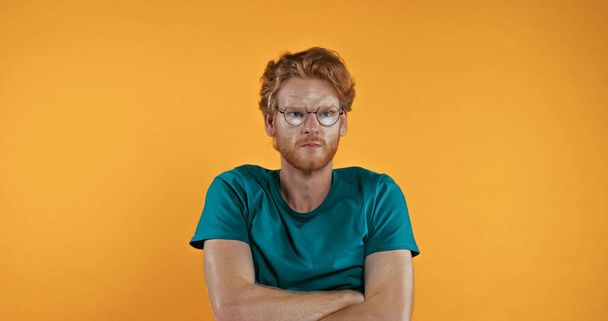 offended redhead man in glasses standing with crossed arms isolated on yellow - Photo, Image