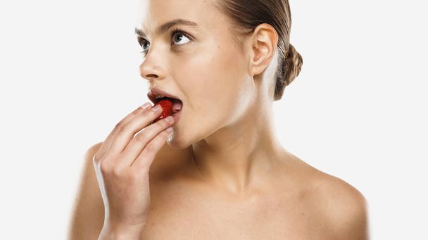 young woman with bare shoulders eating strawberry isolated on white - Photo, Image