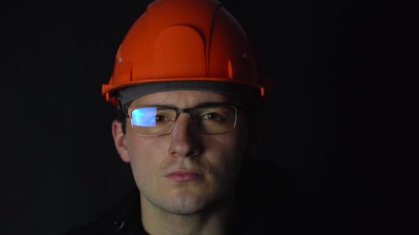 een man met een bril en een helm die op een donkere achtergrond naar de camera kijkt - Video