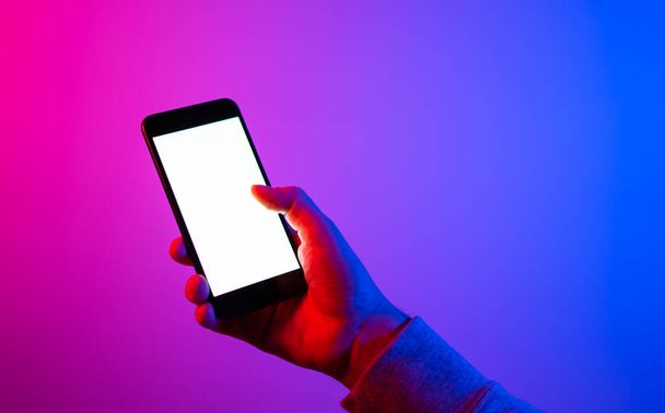 Männliche Hand mit Smartphone. Leere weiße Leinwand. Attrappe. Rotes und blaues Neonlicht. - Foto, Bild