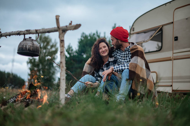 Paar in een geruite ruitjes roosteren marshmallows in brand in de buurt van de trailer huis. - Foto, afbeelding