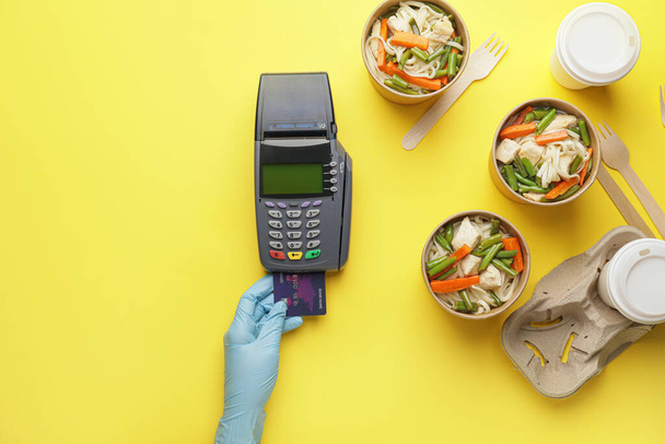 Female hand with credit card, payment terminal and noodles in boxes on color background - Photo, Image