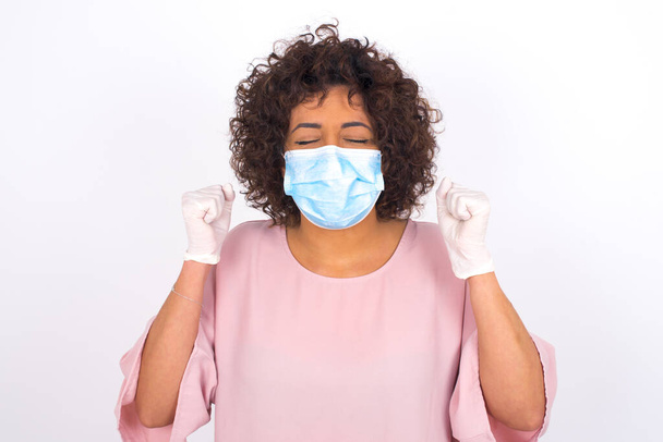 young woman in face mask with fists isolated on white background. Protection against infectious disease. Young woman dressed in casual clothes posing in studio - Photo, Image