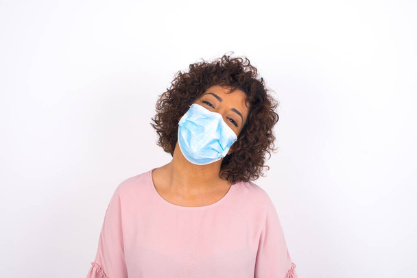 young woman in face mask is happy isolated on white background. Protection against infectious disease. Young woman dressed in casual clothes posing in studio - Photo, Image