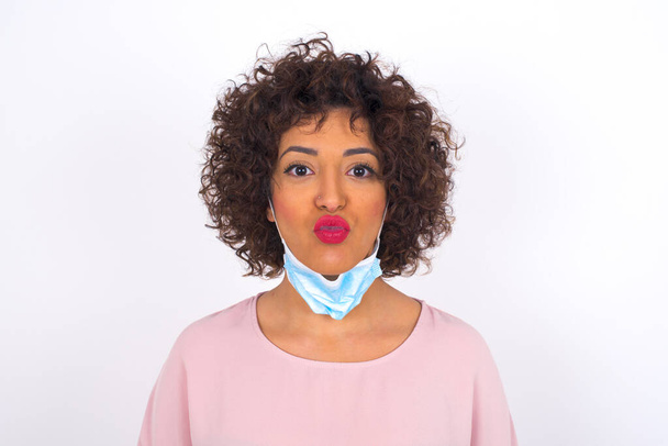 giovane donna in maschera che mostra bacio isolato su sfondo bianco. Protezione contro le malattie infettive. Giovane donna vestita in abiti casual in posa in studio - Foto, immagini